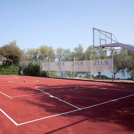 โดลเช บาย วินด์แฮม อัตติกา ริเวียรา Hotel วราโวนา ภายนอก รูปภาพ The photo shows a basketball court with a reddish surface. There are two basketball hoops on either side of the court, surrounded by a fence that has banners displaying the word "ZEUS." In the background, there are trees, and the court appears to be 